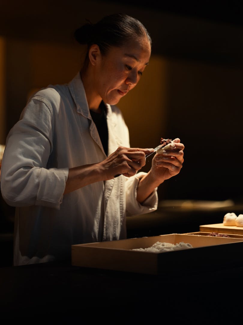 A shop assistant wrapping a box of wagashi, traditional Japanese pastries, in white paper. 